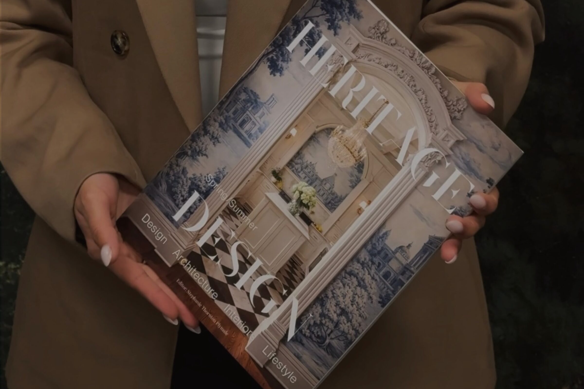 Heritage Design Magazine displayed by a person wearing a neutral tailored blazer.